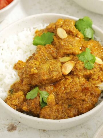 A white bowl containing creamy lamb curry with rice and garnished with almond flakes and coriander.