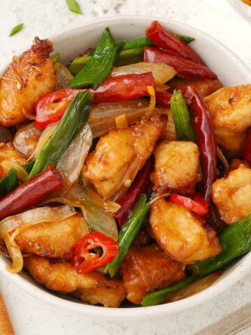 A white bowl containing, crispy coated chicken with dried chillies and spring onions.