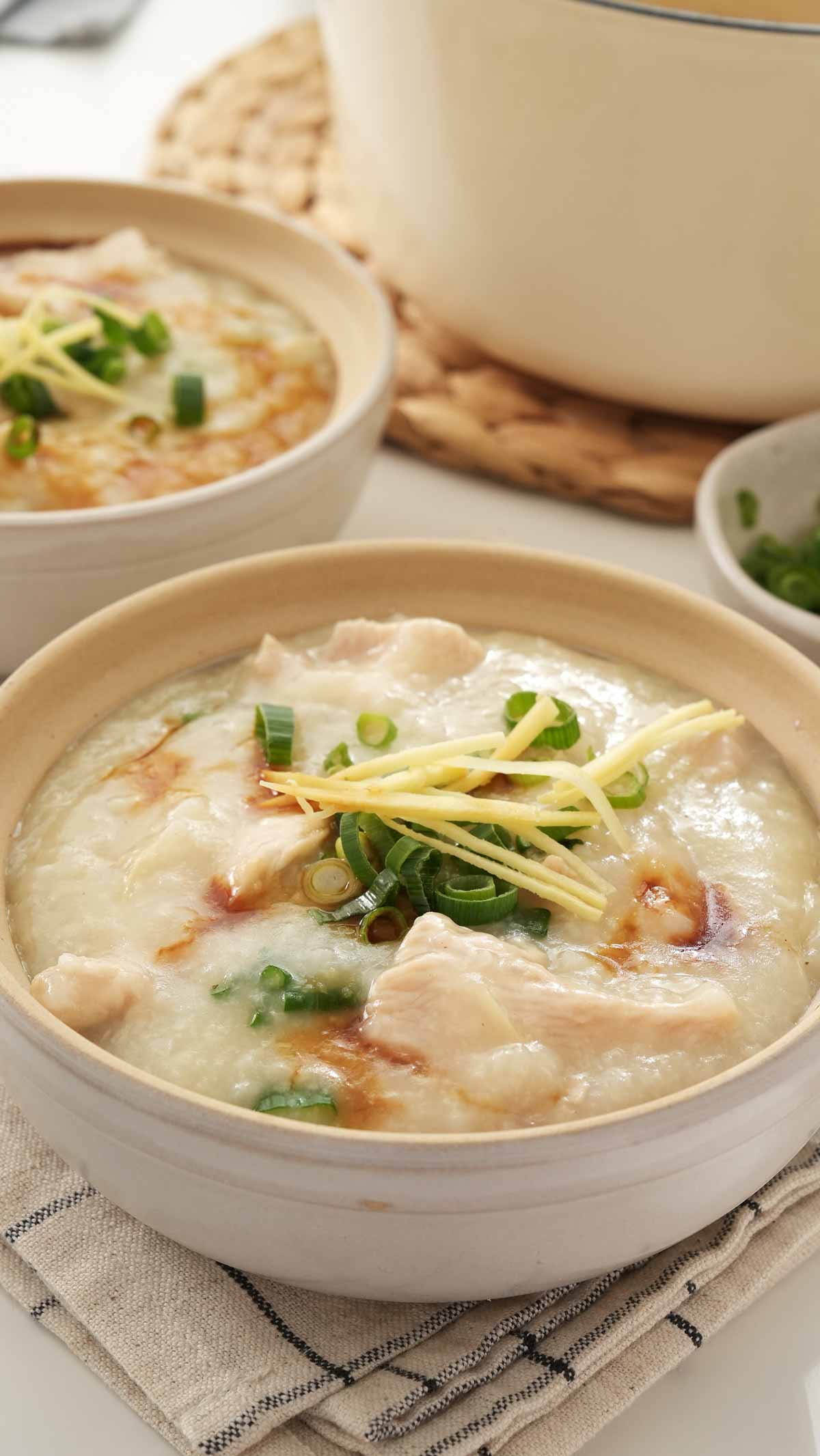 White colour Chinese clay serving bowl containing, rice porridge with chicken, ginger, and spring onions. 