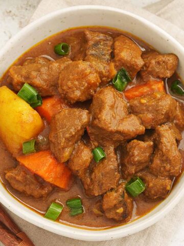 A white bowl containing, small beef cubes , carrots, potatoes with light brown colour curry sauce.