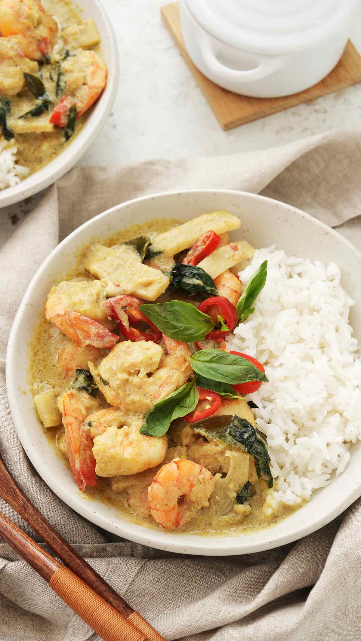 A white plate containing prawns, bamboo shoots, basil leaves, and red chillies with white rice on the side. 