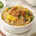 A white bowl containing crispy fried garlic, egg, rice and green onions.
