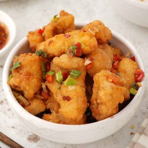 A white bowl containing, coated fried fish pieces with spring onions and chilli flakes.