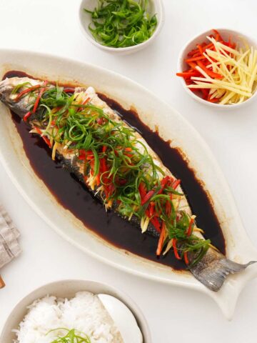 A white plate containing Chinese-style whole steamed fish with ginger, chilli, and scallions.