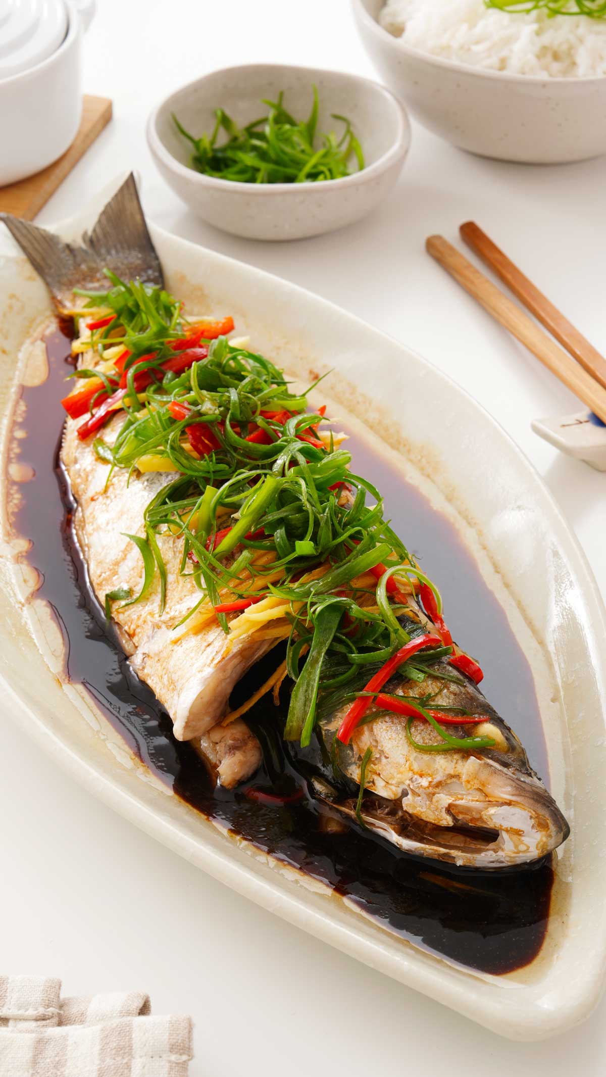 A white plate containing steamed whole fish with sauce and shredded vegetables. 