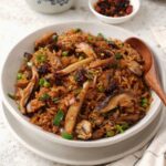 A white bowl containing, fried rice with mushrooms, spring onions, and green peas.