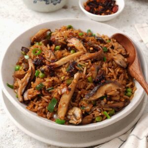A white bowl containing, fried rice with mushrooms, spring onions, and green peas.
