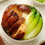 A small serving bowl containing, rice, soy sauce chicken pieces, and blanched pak choi.