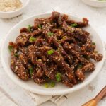 A white plate containing beef with sesame seeds and spring onions.