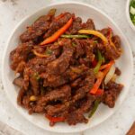 A picture of beef strips with bell peppers, onions, and sweet and sour sauce.