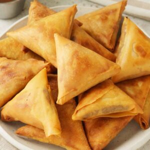 A white plate containing golden colour deep fried samosas with keema and vegetables.