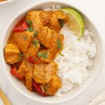 A serving bowl containing peanut butter chicken with rice on the side.
