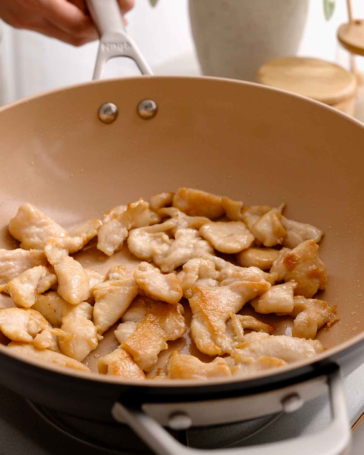 An image showing how to stir fry chicken in a large wok.