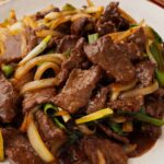 A white plate containing beef stir fry with onions and green onions.