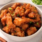 A white bowl containing bite-sized coated fried chicken pieces with sweet chilli sauce.