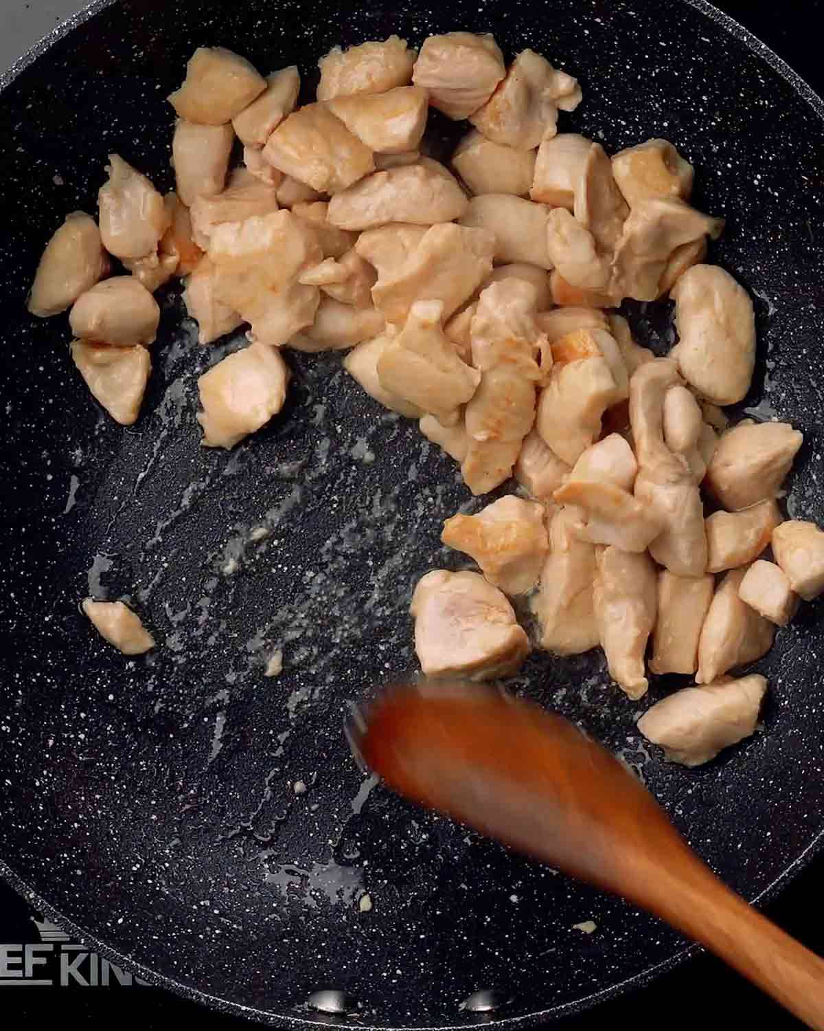 A photo of stir frying chicken pieces in a wok.