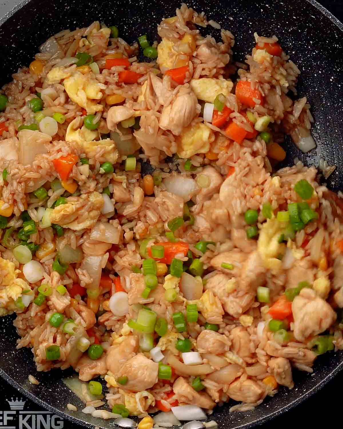 Fried rice with chicken, egg, and vegetables in a black wok.