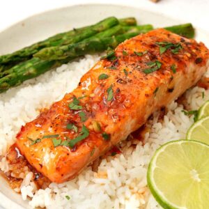 A picture of sweet chilli glazed salmon fillets garnished with coriander, placed over the a bed of white rice.