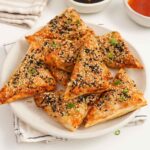 A white plate containing triangle shaped air fryer prawn toast with sesame seeds on top.