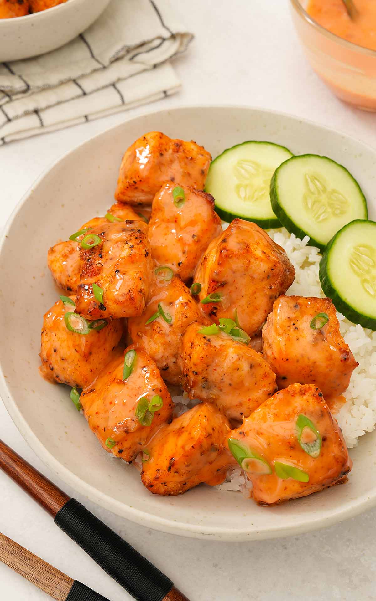 Air-fried salmon bites with bang bang sauce and spring onions, placed over a bed of rice.
