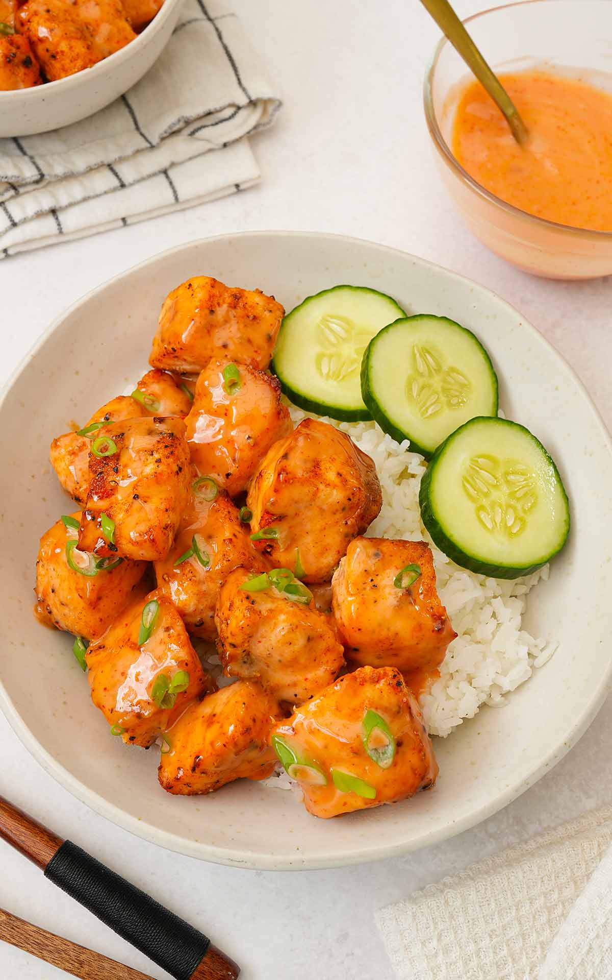 A serving bowl containing rice, fried salmon bites with creamy sauce, and cucumber slices.