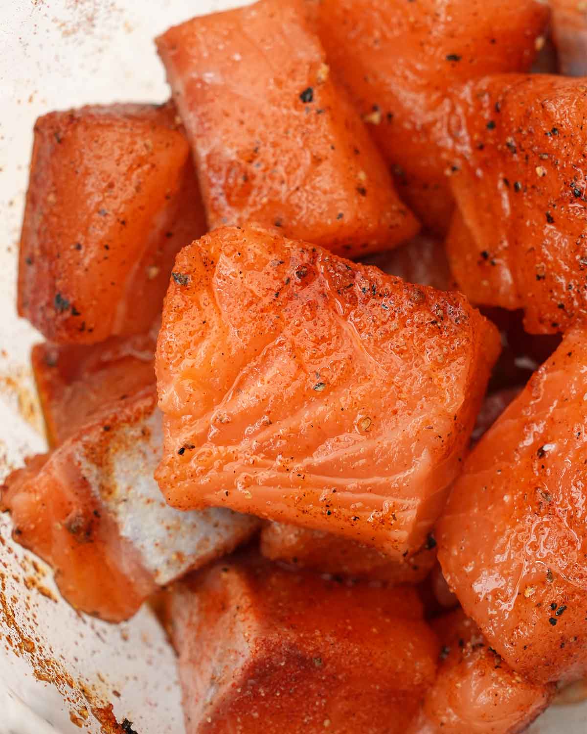 A large bowl containing salmon pieces mixed with seasoning spices.