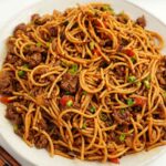 A white plate containing ground beef, noodles, spring onions, and chillies.