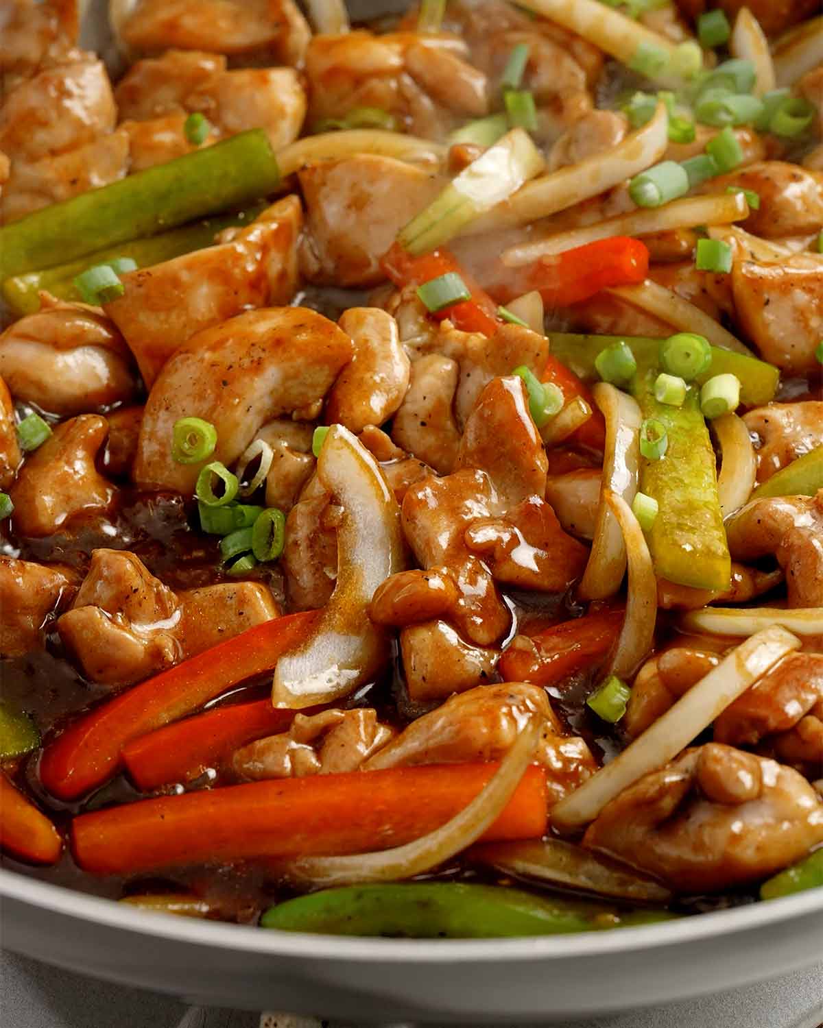 A picture of stir frying chicken and vegetables with glossy black pepper sauce in a black pan.