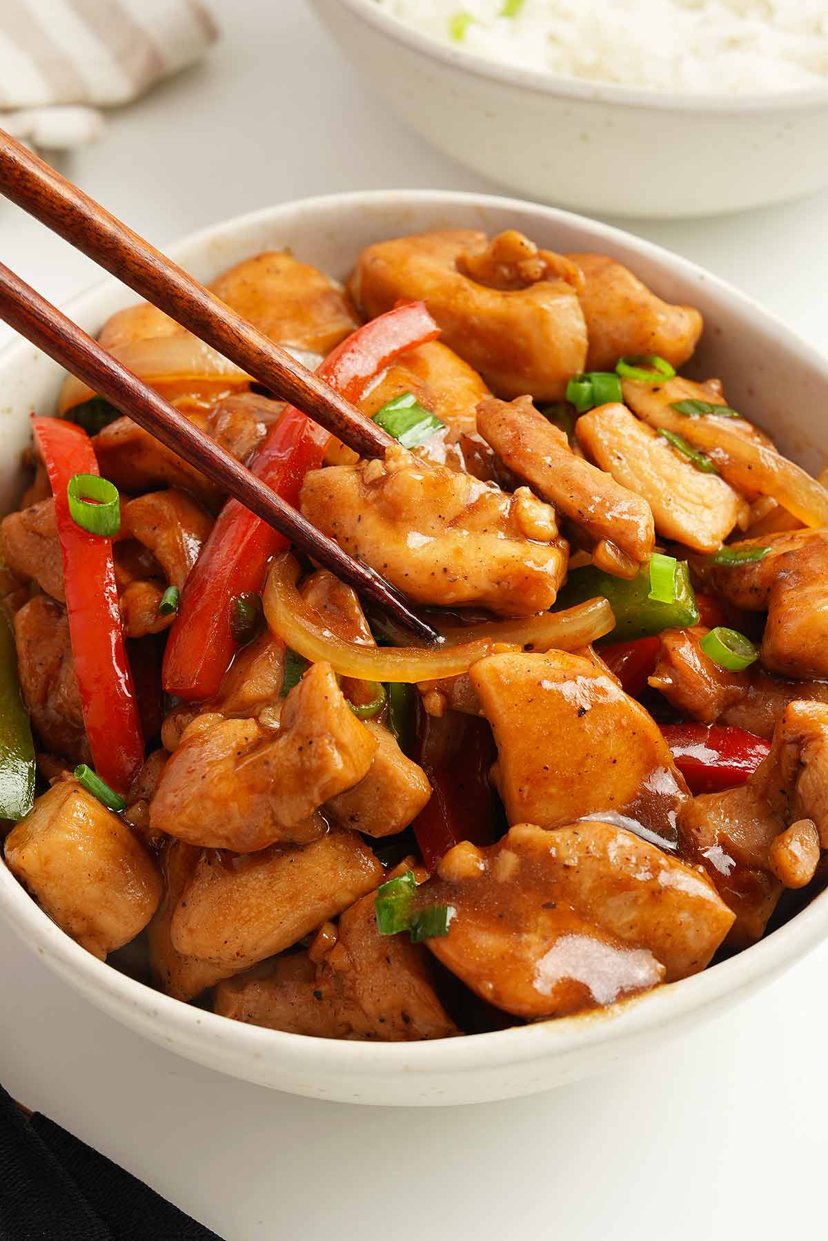 A white bowl containing stir fried chicken pieces with vegetables and Chinese black pepper sauce.