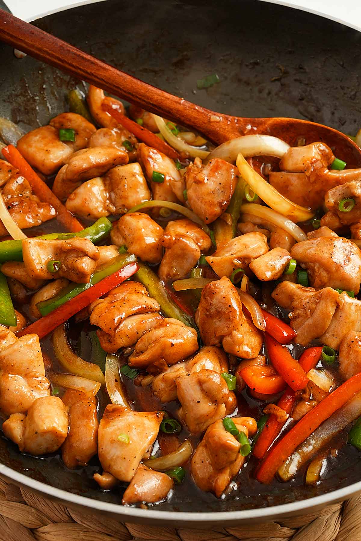 A black pan containing Chinese black pepper chicken with bell peppers and onions with glossy brown sauce.
