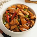A white bowl containing stir fried chicken, vegetables, and glossy black pepper sauce.