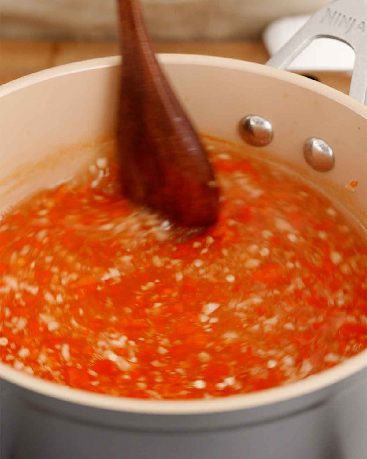 A picture of a saucepan containing chilli sauce ingredients and stirring with a wooden spoon. 