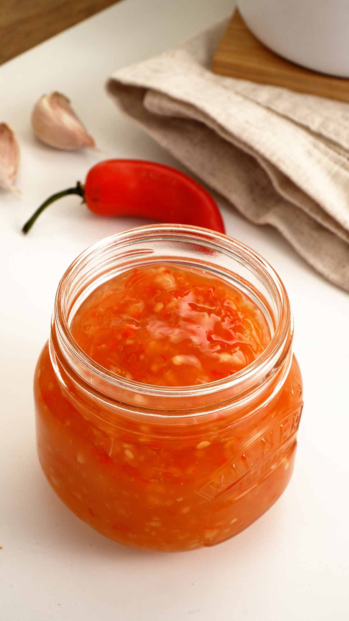An image of a glass jar containing sweet chilli sauce with garlic and chilli flakes.