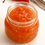 A clear glass jar containing glossy sweet chilli sauce.