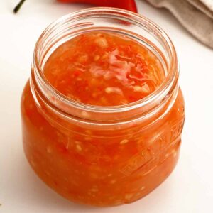 A clear glass jar containing glossy sweet chilli sauce.