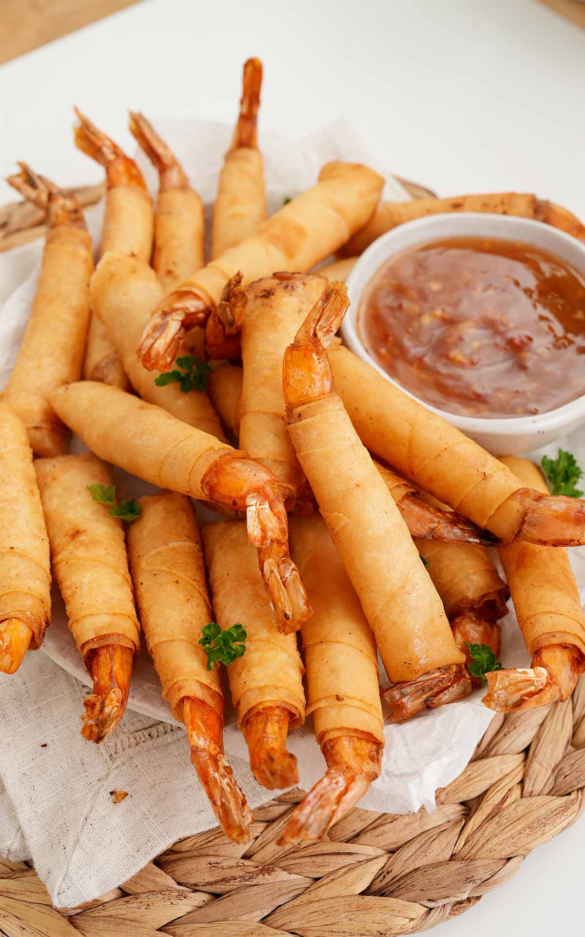 A white plate containing, fried golden firecracker shrimp spring rolls with dipping sauce on the side.