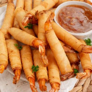 A large plate containing fried golden firecracker shrimp rolls with dipping sauce on the side.