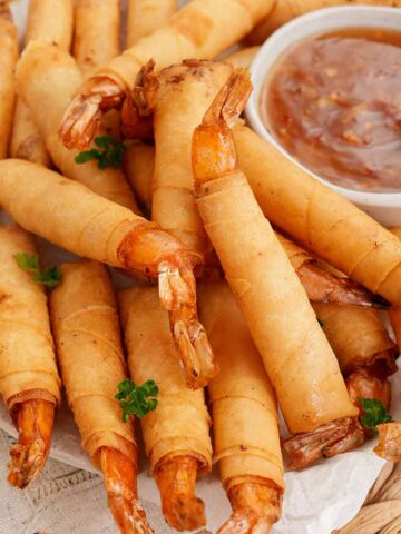 A large plate containing fried golden firecracker shrimp rolls with dipping sauce on the side.