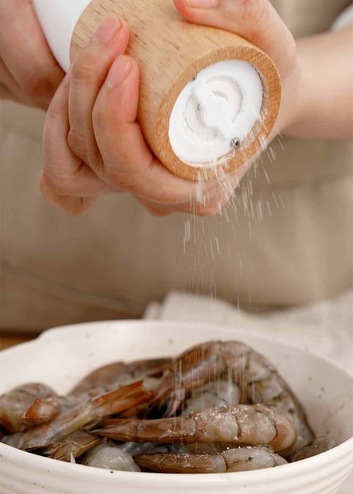 A white bowl containing peeled, deveined shrimps and seasoning ingredients. 