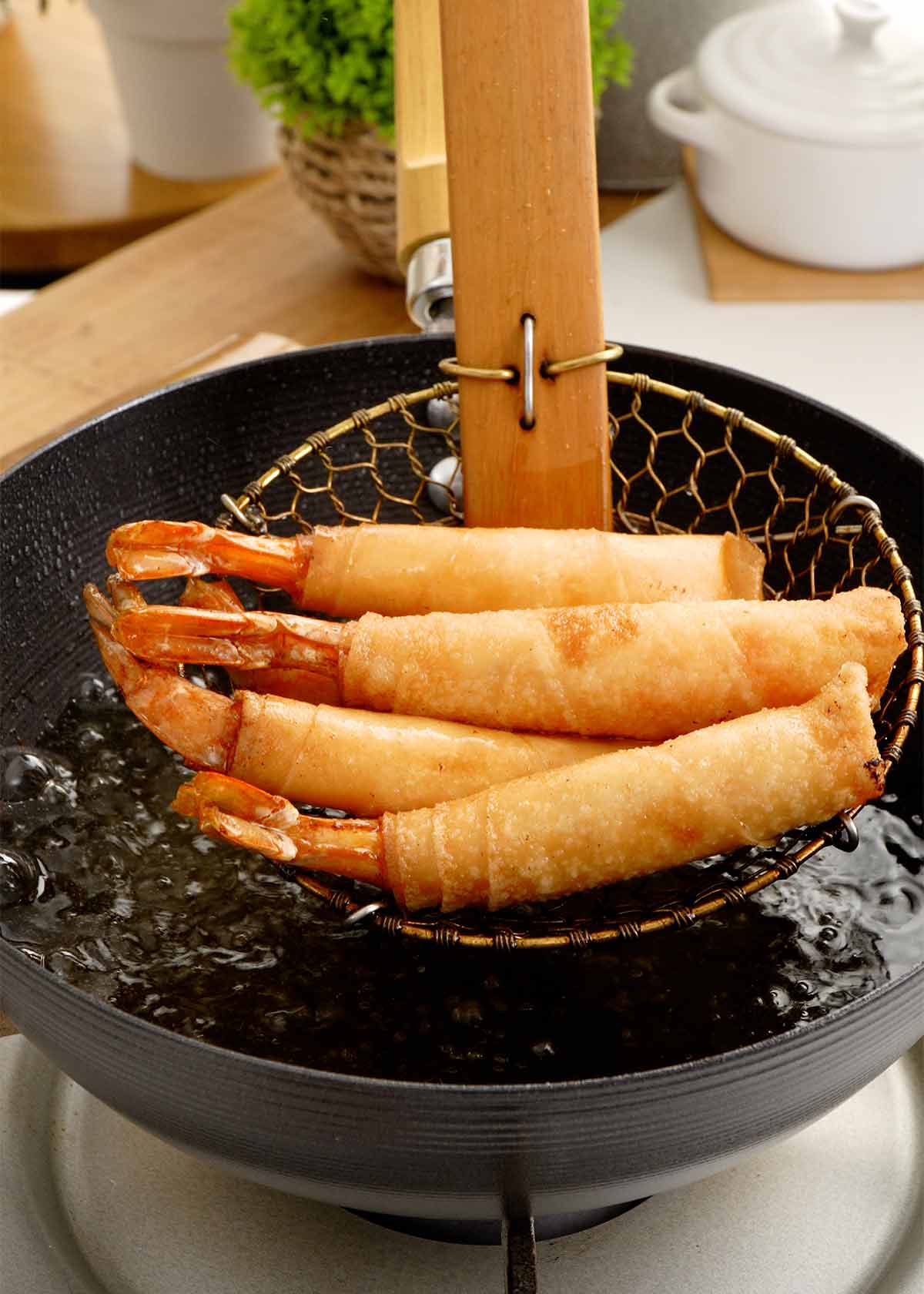 Fried golden firecracker shrimp spring rolls in a frying strainer. 