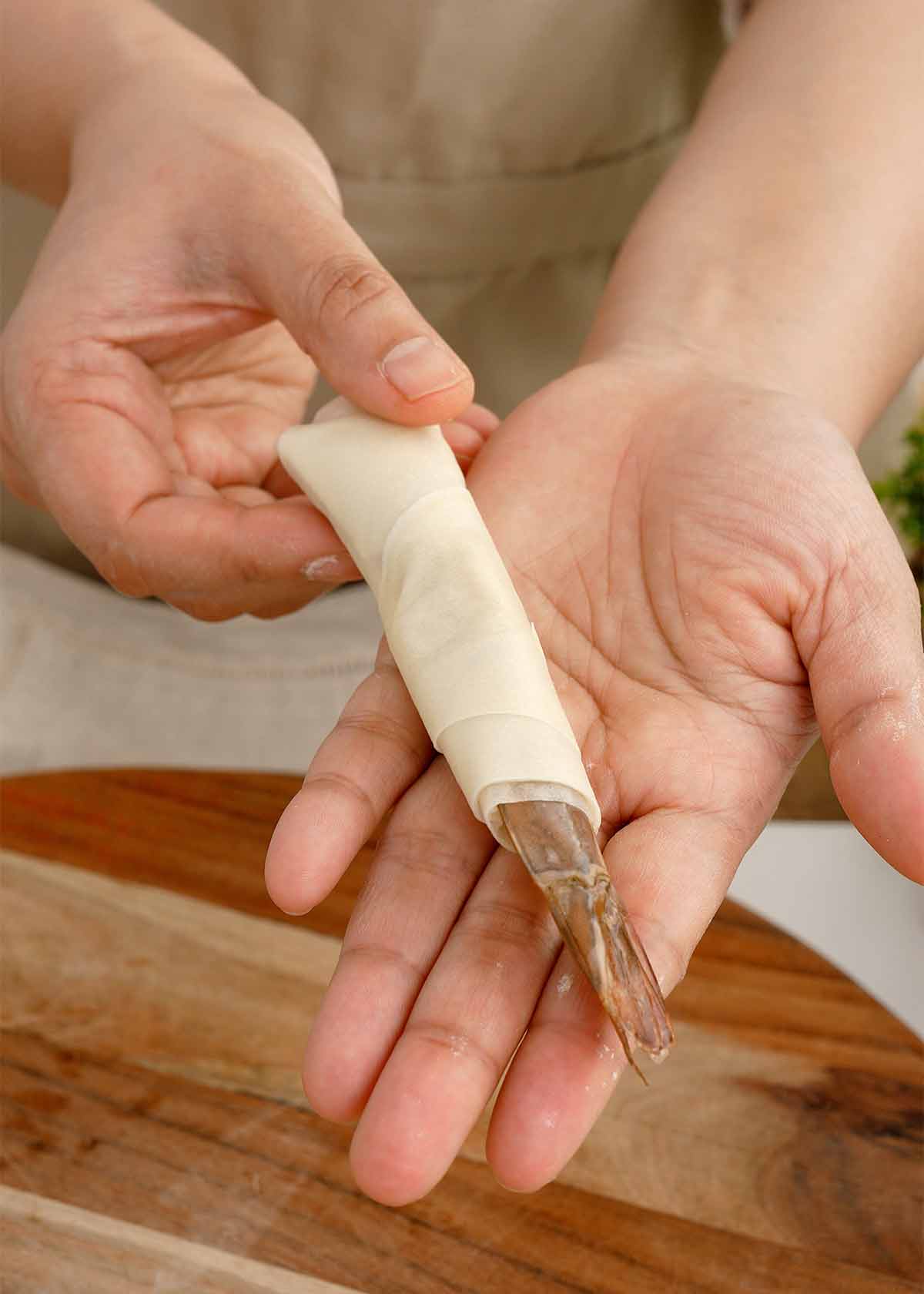 A pair of hands showing the wrapped shrimp in a spring roll sheet. 