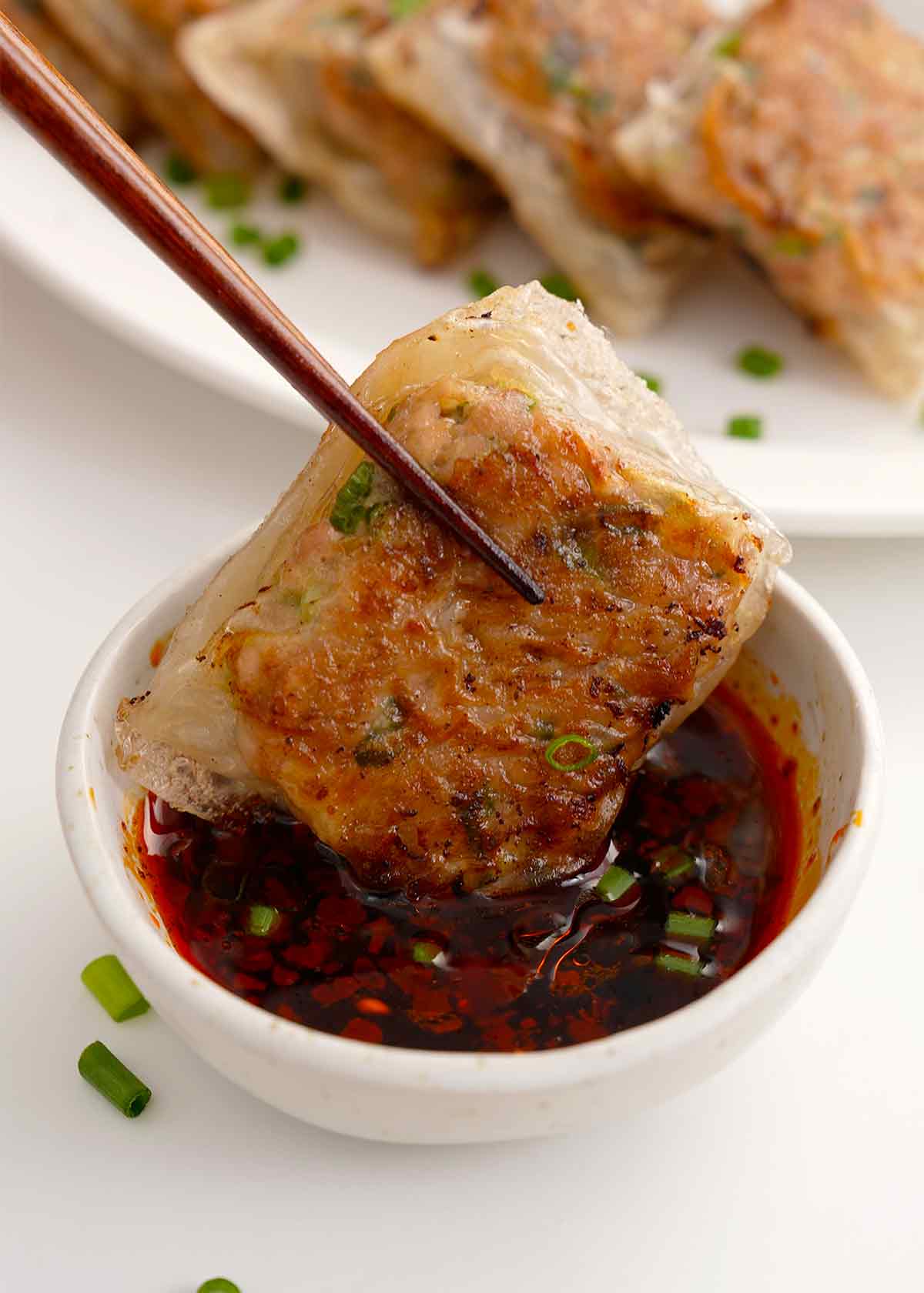 A photo of fried rice paper dumplings dipping in the sauce.