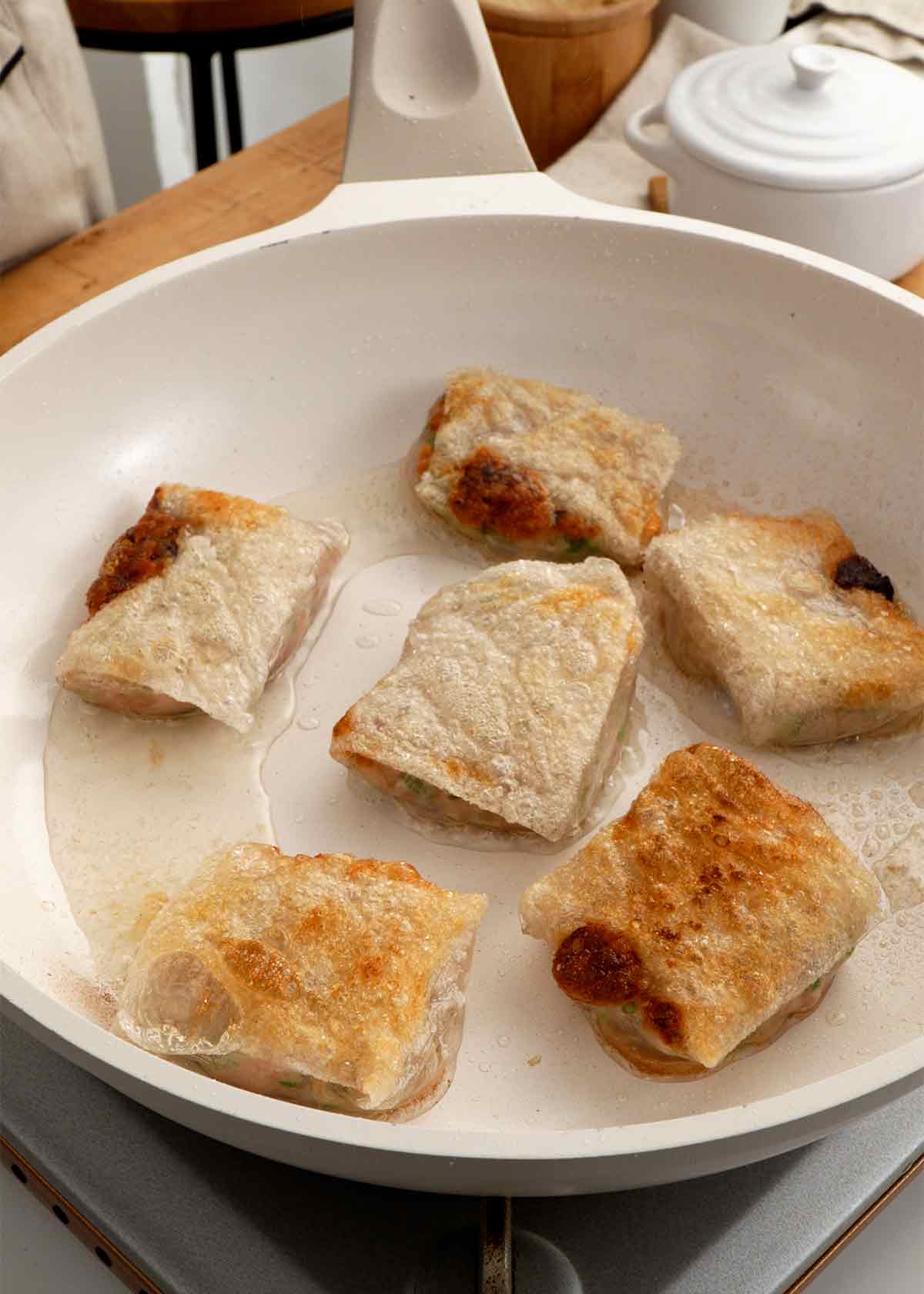 An image showing how to pan fry the dumplings in the white non-stick pan.