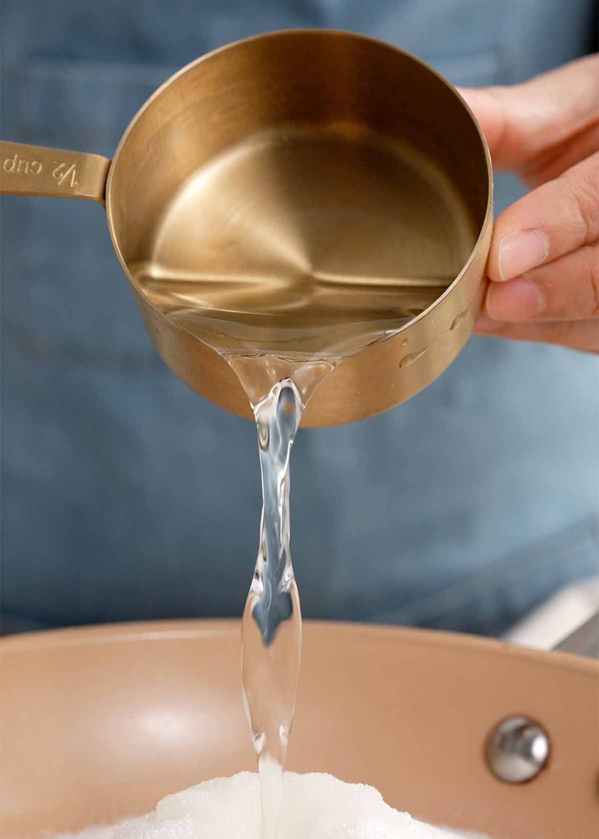 A picture of pouring water into the saucepan containing white sugar. 