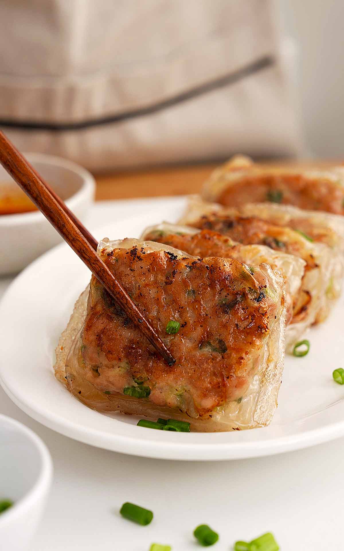 A photo showing a pair of chopsticks holding a rice paper chicken dumpling.