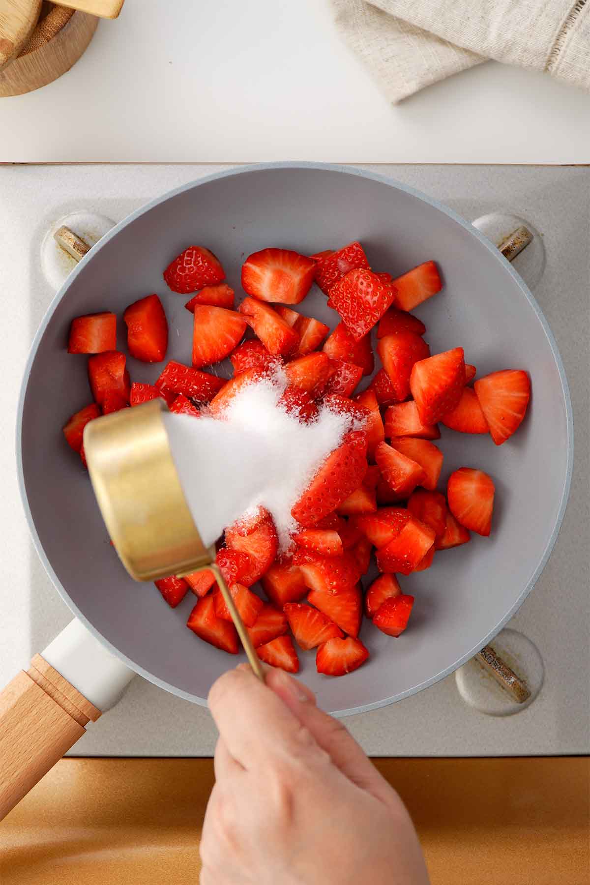 A picture showing combining sugar and strawberries in a saucepan. 