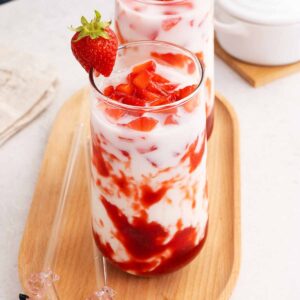 A picture of a tall glass with 3 layers strawberry milk with syrup, milk, and fresh strawberry chunks.