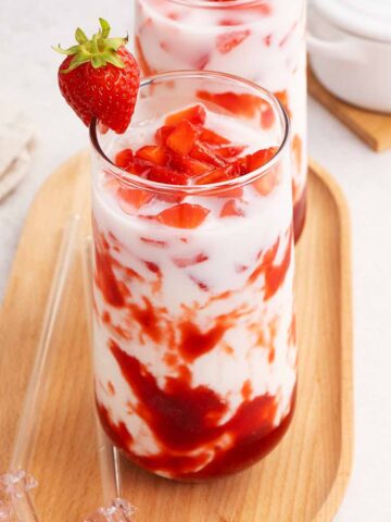 A picture of a tall glass with 3 layers strawberry milk with syrup, milk, and fresh strawberry chunks.