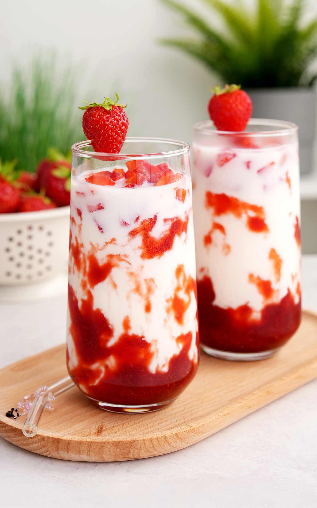 An image of 2 tall glasses containing, strawberry milk decorated with strawberry chunks on top.