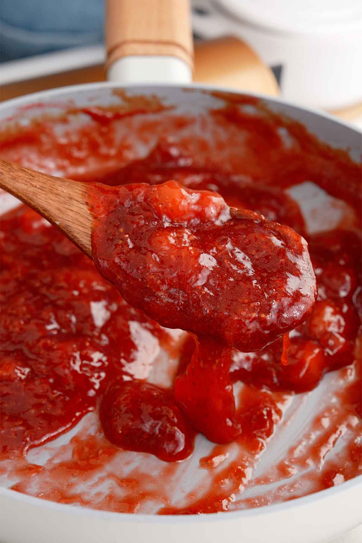 An image showing the consistency of strawberry sugar syrup with a wooden spoon. 
